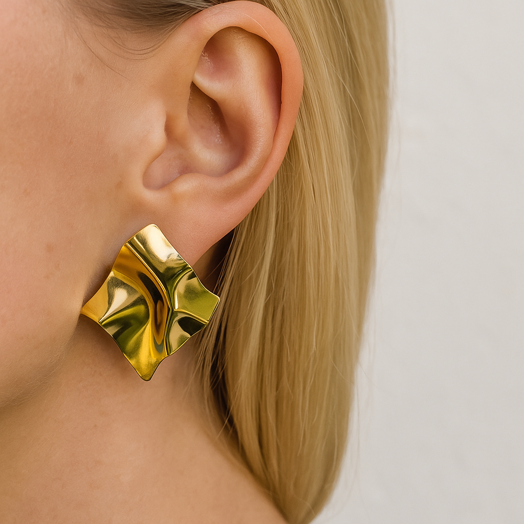 Gold earring worn by a person with a plain background